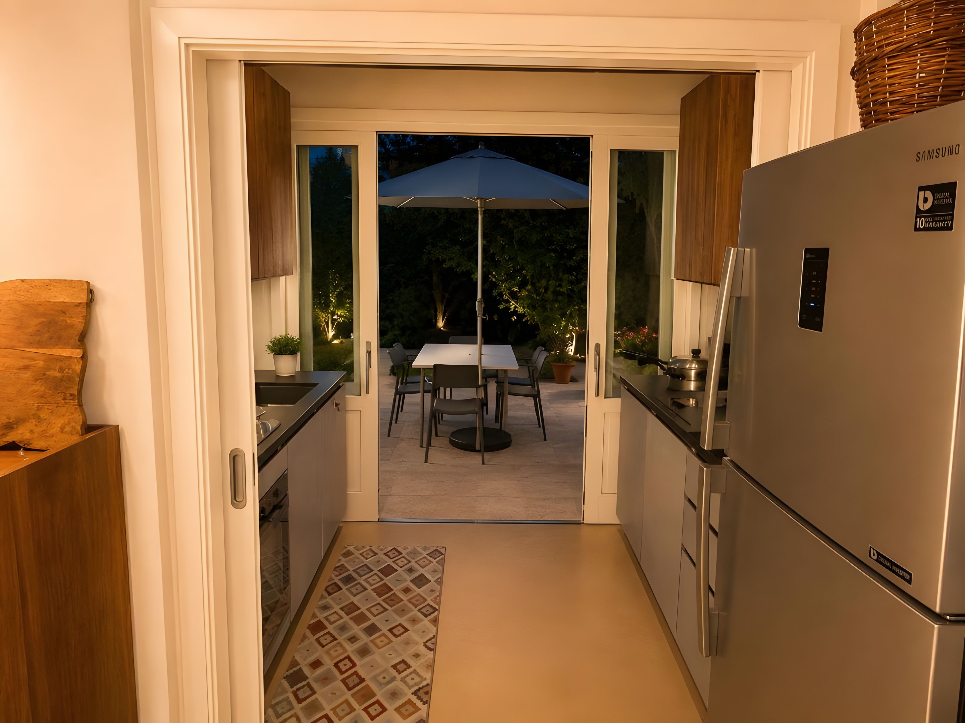 Eine Küche mit Kühlschrank, einem Esstisch mit Stühlen und einem Sonnenschirm draußen.