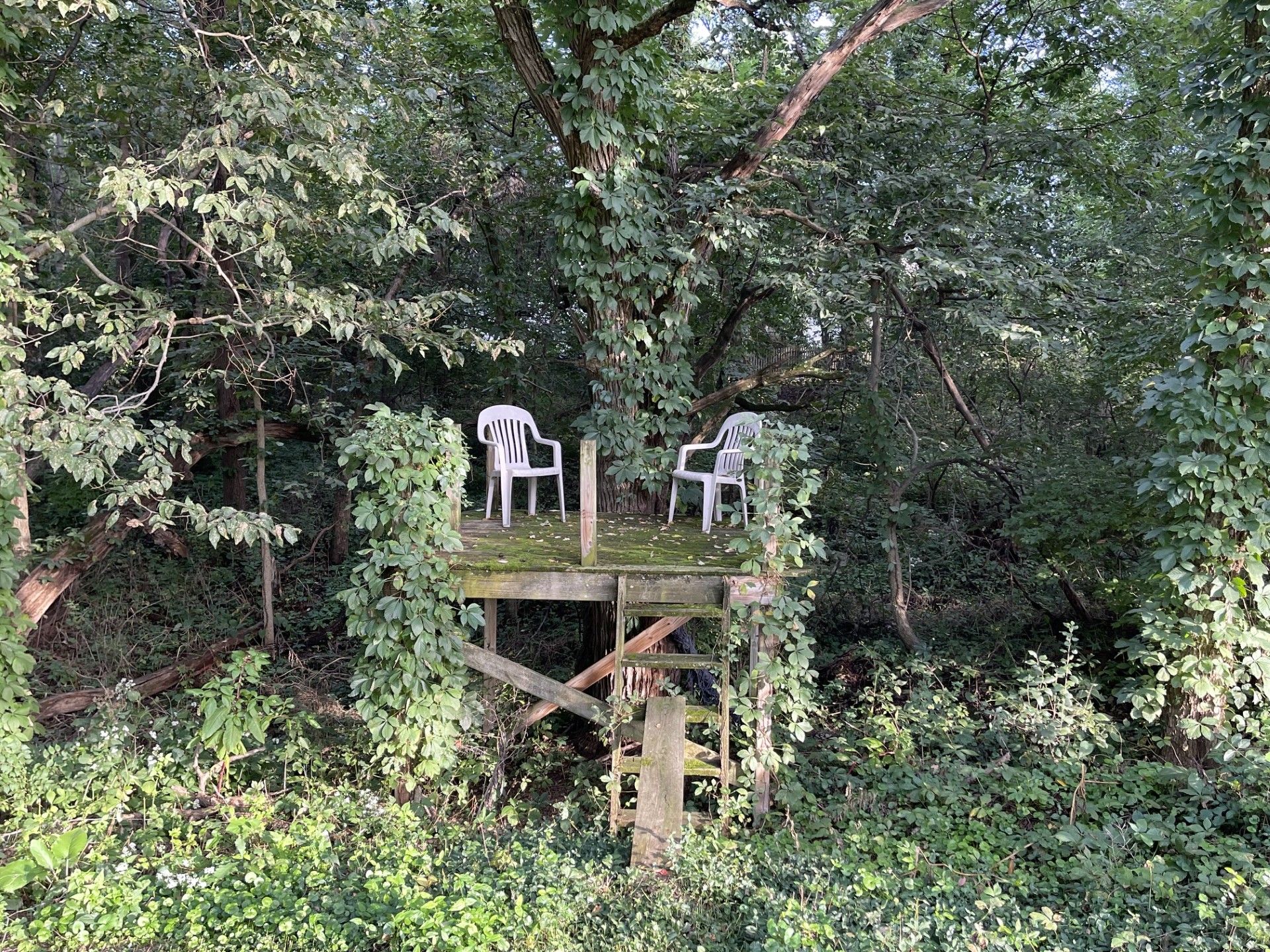 A wooden treehouse with two white plastic chairs.