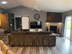 Een moderne woonkamer met een modulaire bank, een flatscreen televisie, een open haard en een plafondventilator.