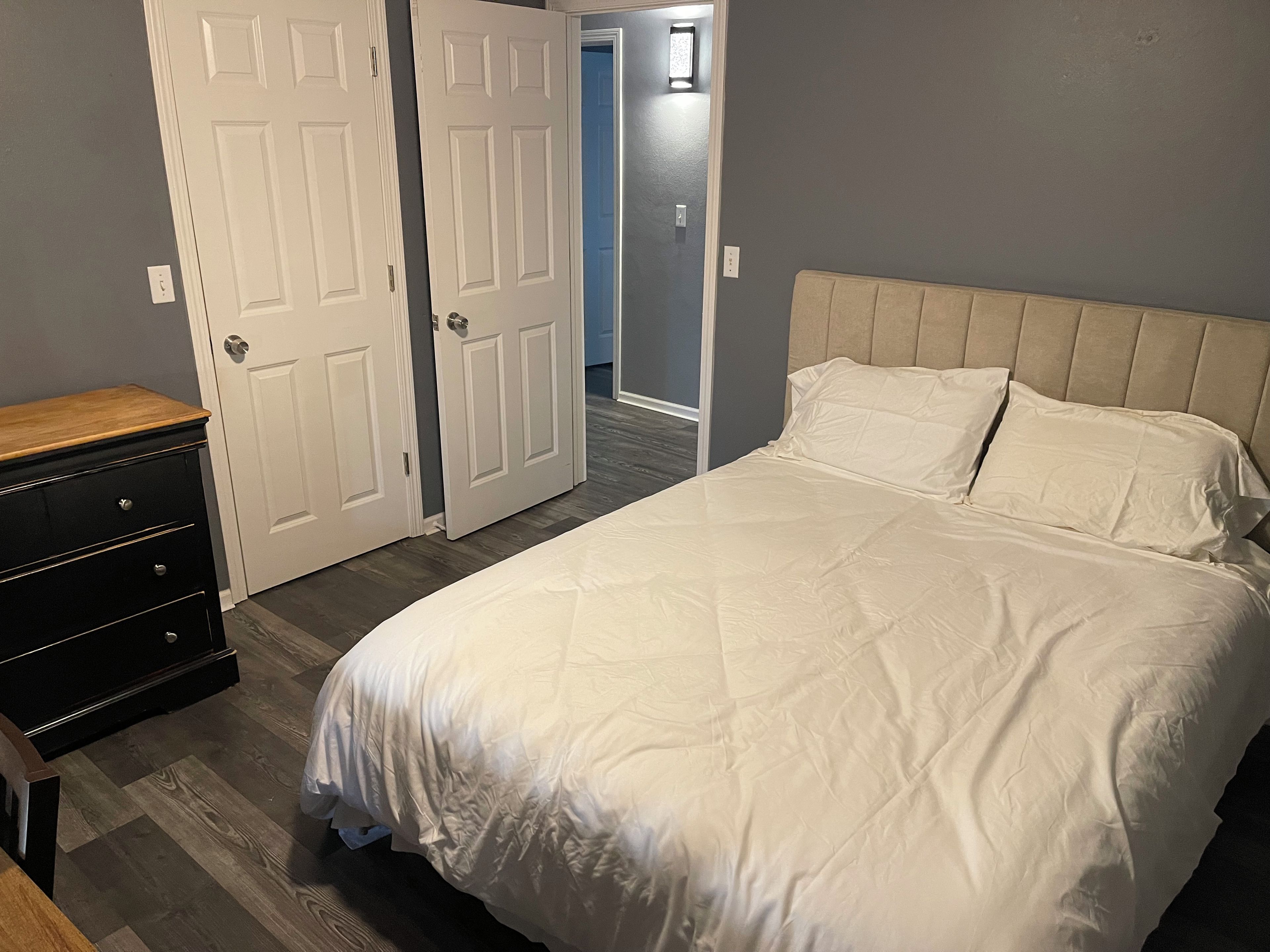 Ein Schlafzimmer mit einem Bett, einer Kommode und einer Tür zu einem weiteren Raum.