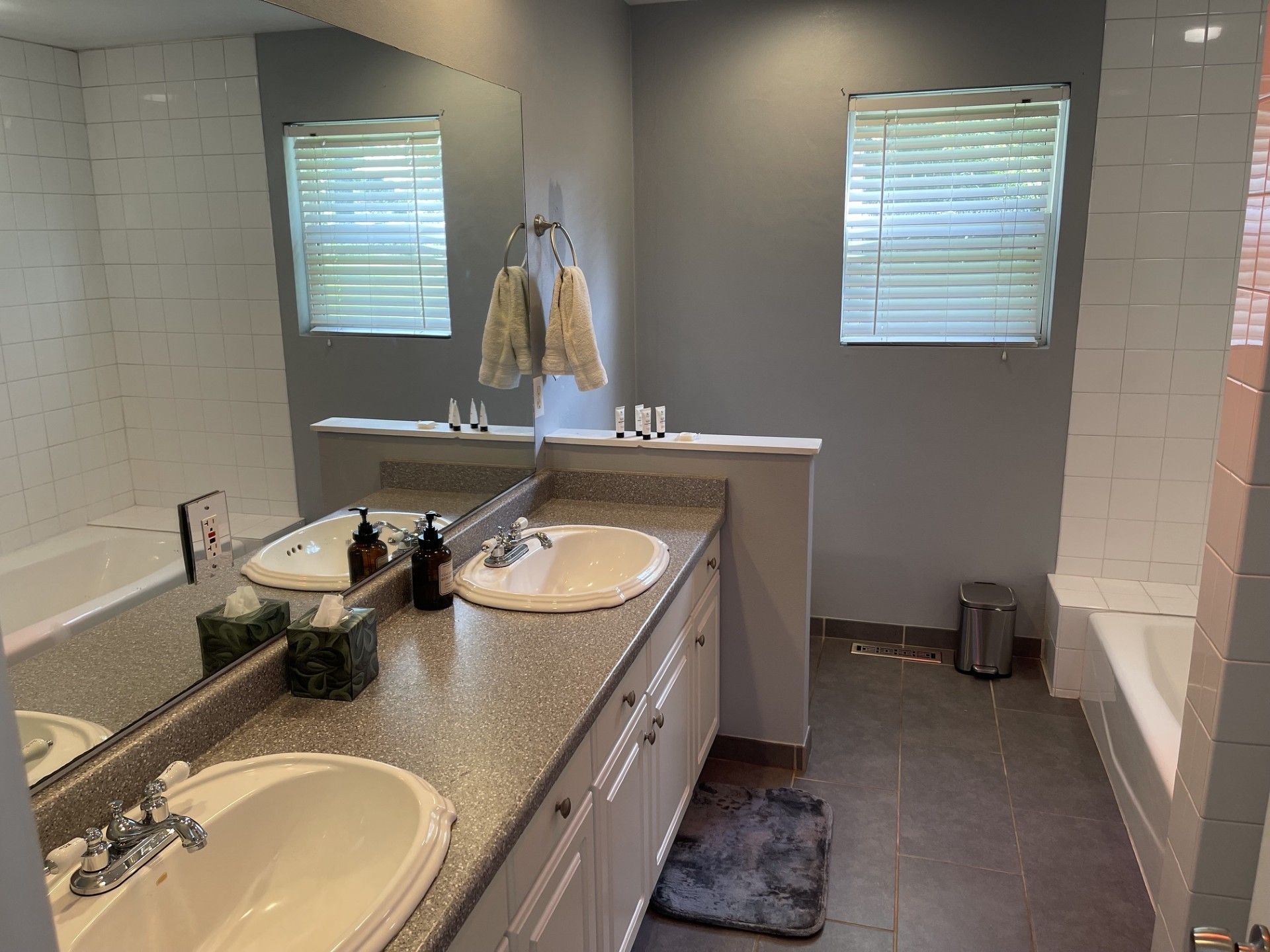 A bathroom with two sinks, a mirror, a towel rack, and a window with blinds.