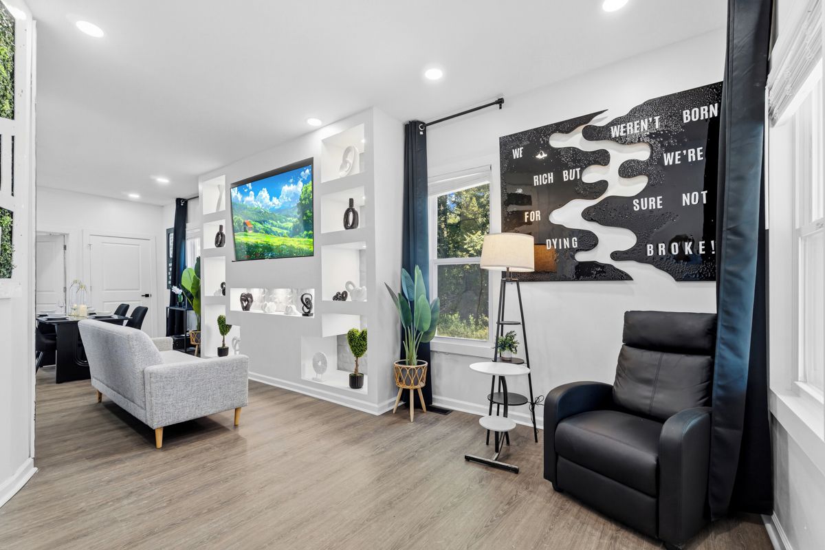 Un salon moderne avec un canapé gris, un fauteuil en cuir noir, un grand téléviseur et une œuvre d’art murale inspirante.
