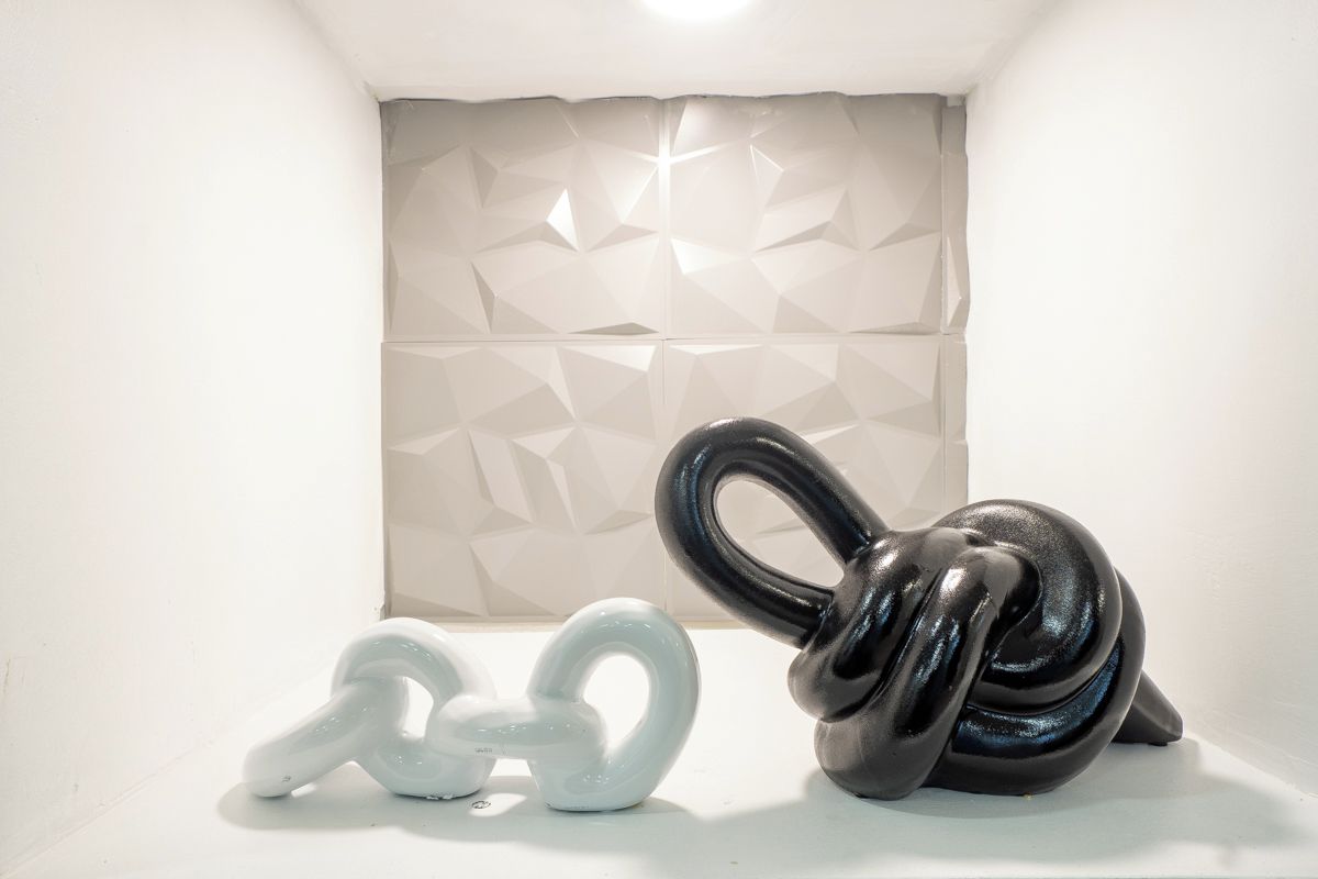 A white wall with a geometric pattern and two abstract sculptures, one white and one black.
