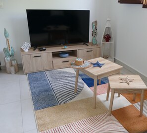 A living room with a television, wooden furniture, decorative items, and patterned rugs. - Les Gîtes d'Anna Blue " Gite Côté Mer " (Sainte-Anne)