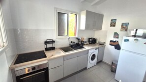 A compact kitchen with a stove, sink, washing machine, and a refrigerator. - Les Gîtes d'Anna Blue " Gite Côté Mer " (Sainte-Anne)