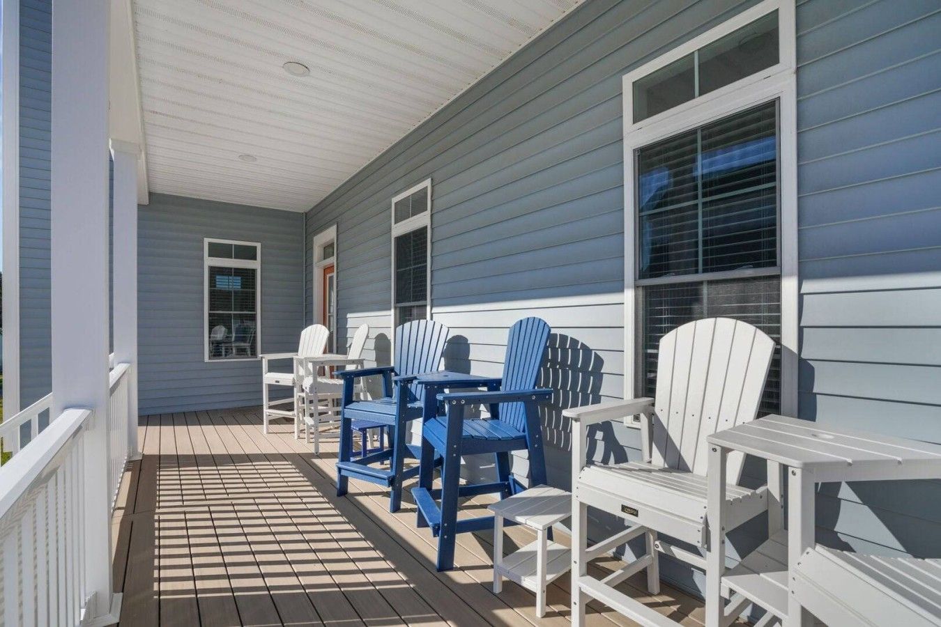 A covered porch with a wooden floor, white railings, and a seating area with blue and white Adirondack chairs.