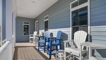 A covered porch with a wooden floor, white railings, and a seating area with blue and white Adirondack chairs.