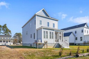 A two-story white house with a front porch, a staircase, and a garage. - The Island House | New Luxury Family Retreat, Spacious, Porch, 2 Decks, & Grill (Chincoteague)