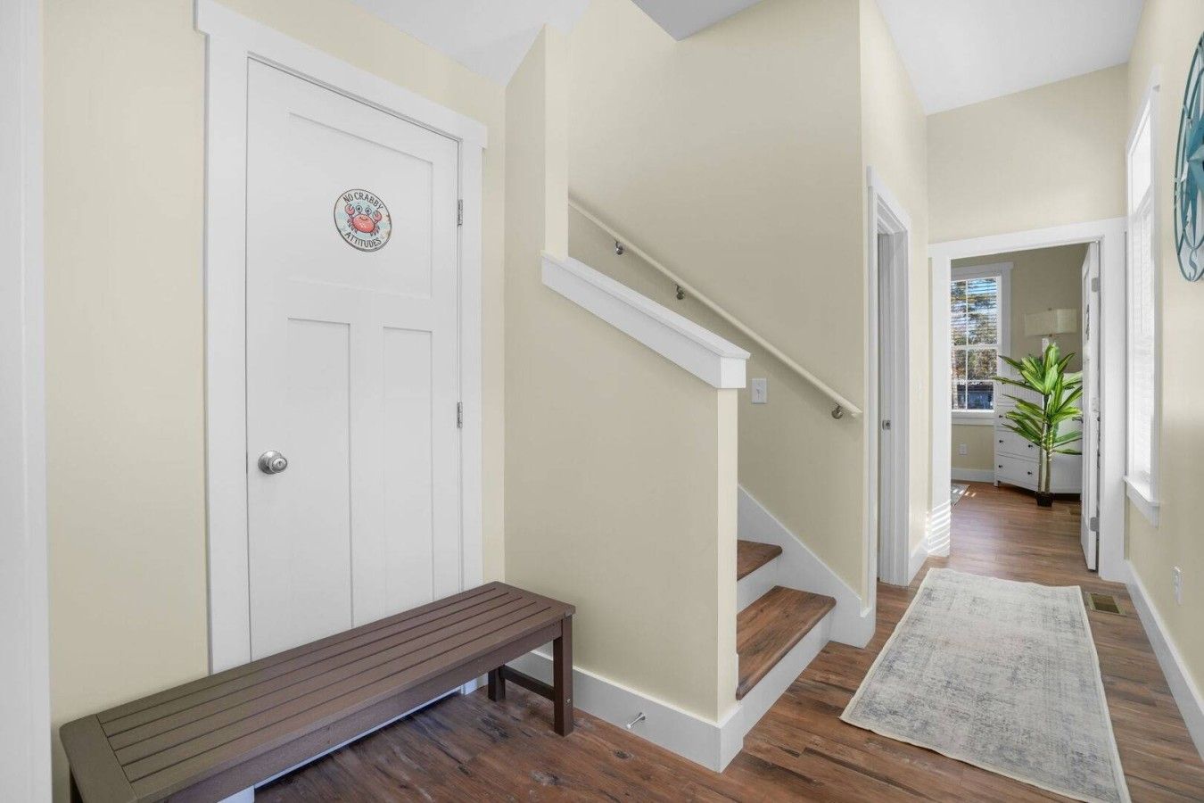 A hallway with a wooden bench, a white door with a sticker, and a staircase.