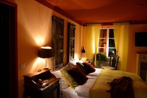 Quarto de hotel com cama, mesa de cabeceira, abajur, cortinas e janela.