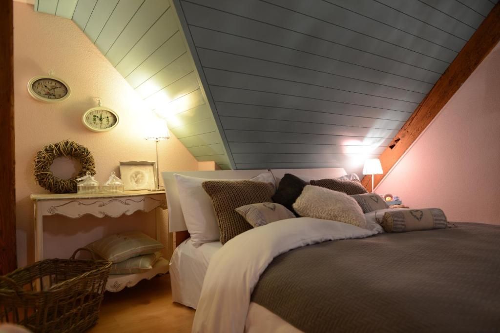 A bedroom with a sloped ceiling, a bed with multiple pillows, a bedside table with a lamp, and a wall clock.