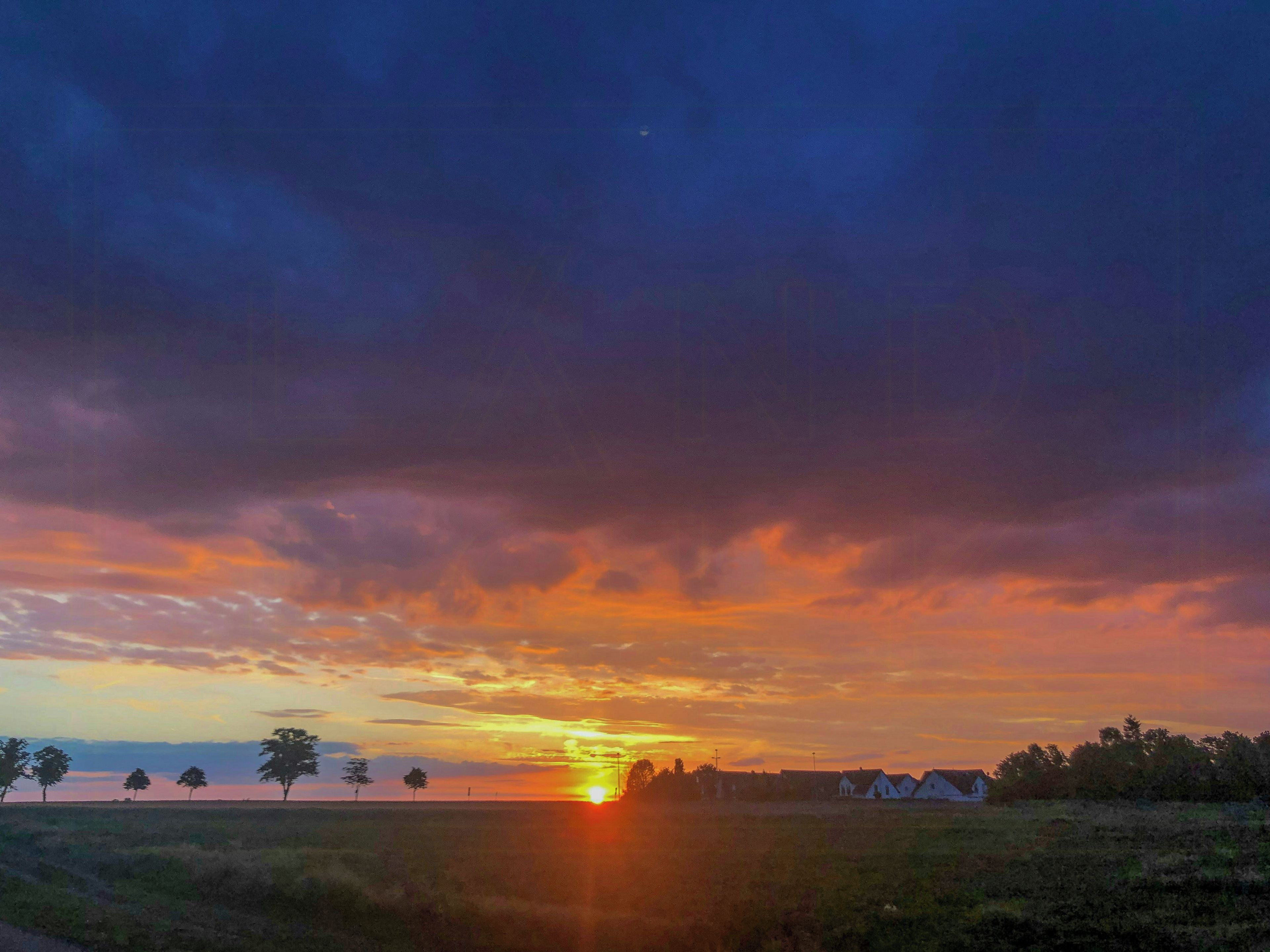 Pôr do sol sobre uma paisagem rural com campos abertos e árvores esparsas.