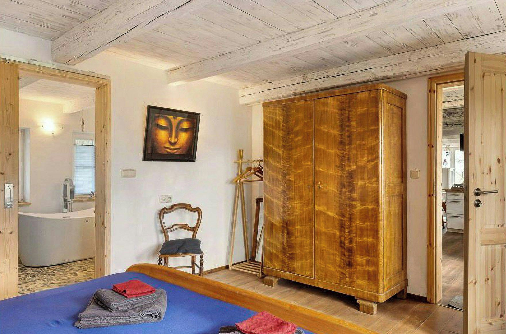 A bedroom with a bed, a wooden wardrobe, a chair, and a painting on the wall.