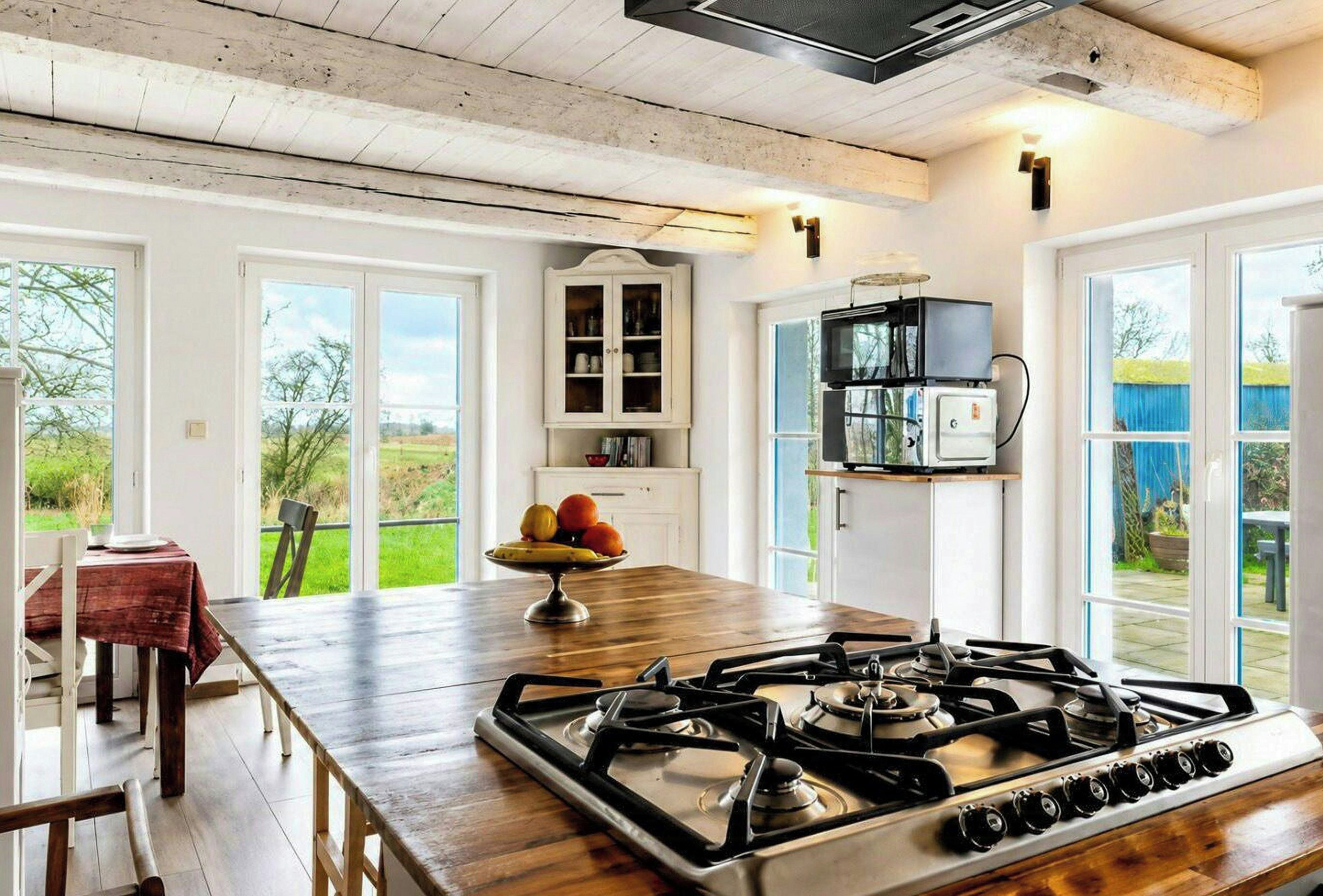 A kitchen with a gas stove, wooden table, and a view of the outdoors.