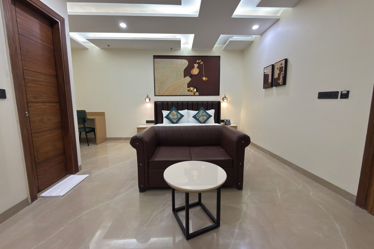 Quarto de hotel moderno com sofá de couro marrom, mesa redonda, cama com cabeceira e obras de arte nas paredes.