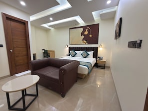 Quarto de hotel moderno com cama, sofá de couro marrom, mesa redonda pequena e obra de arte na parede.