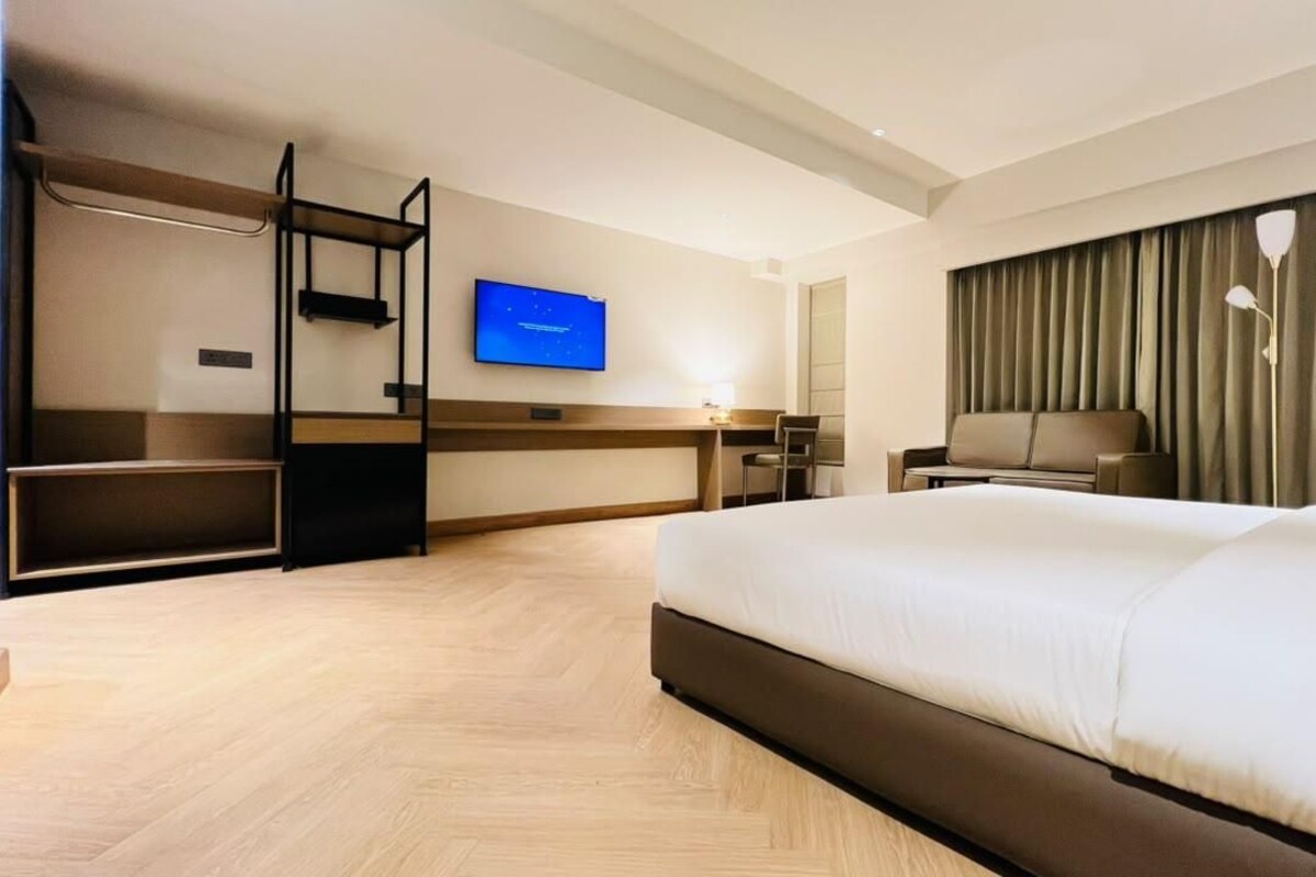 Una habitación de hotel con una cama grande, un escritorio con silla, un televisor y una ventana con cortinas.