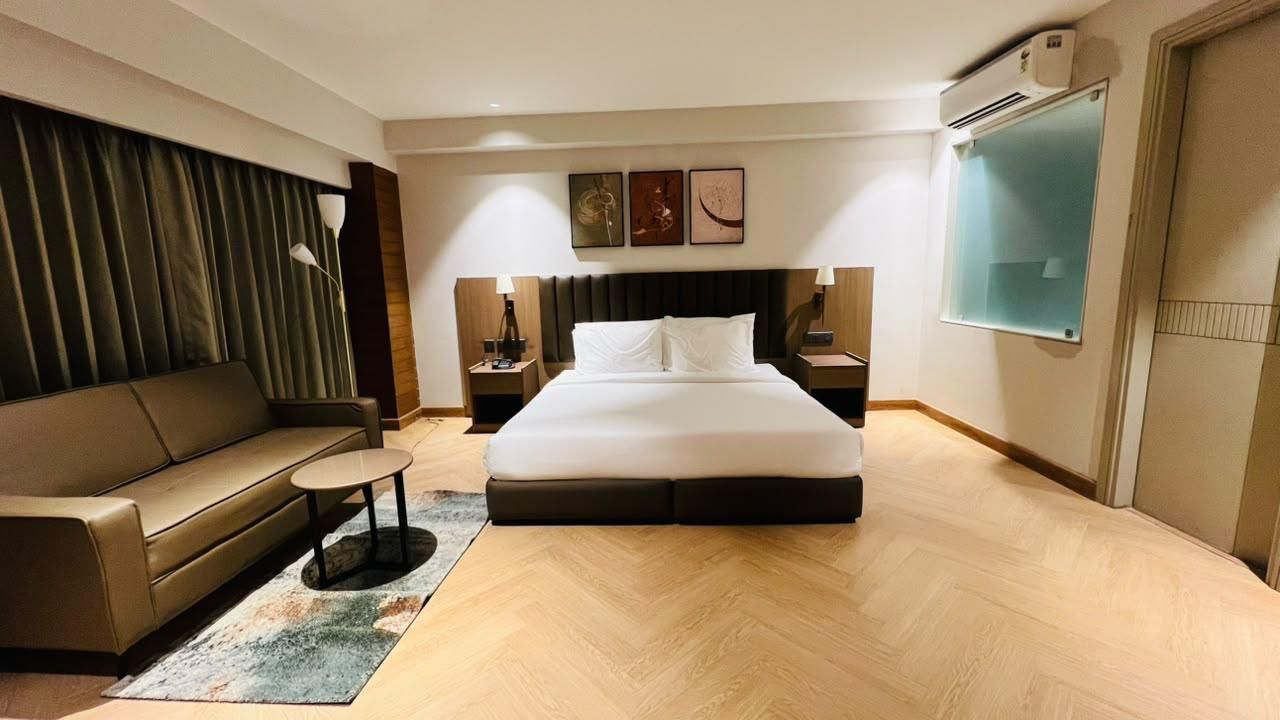 Una habitación de hotel con una cama grande, un sofá, una mesita pequeña y un aire acondicionado instalado en la pared.