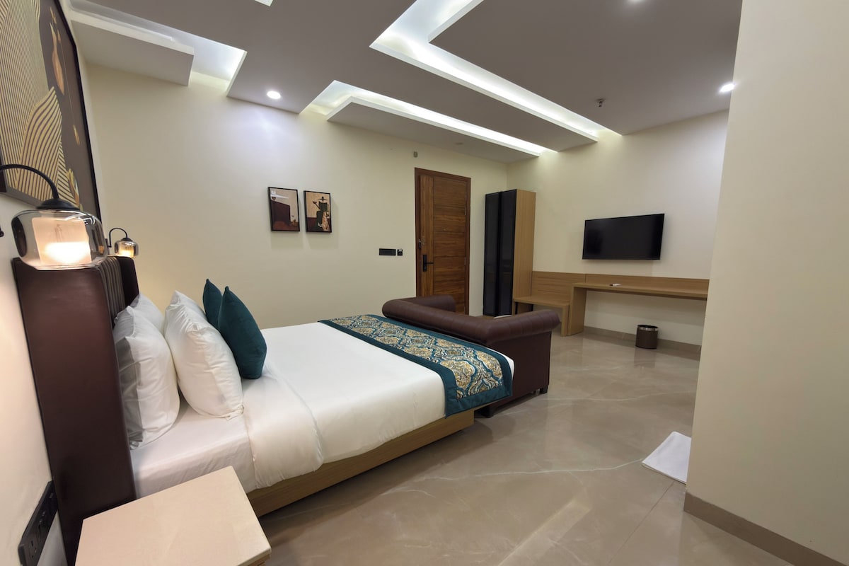 Quarto de hotel moderno com uma cama grande, escrivaninha, TV de tela plana e teto com iluminação embutida.