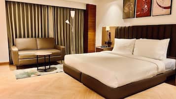 A hotel room with a large bed, a sofa, a small table, and a curtain.