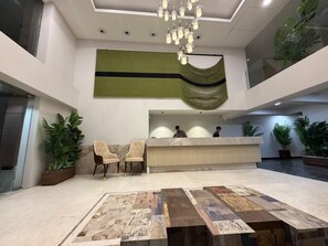 Un área de recepción con piso de mármol, un mostrador, dos sillones y una araña.