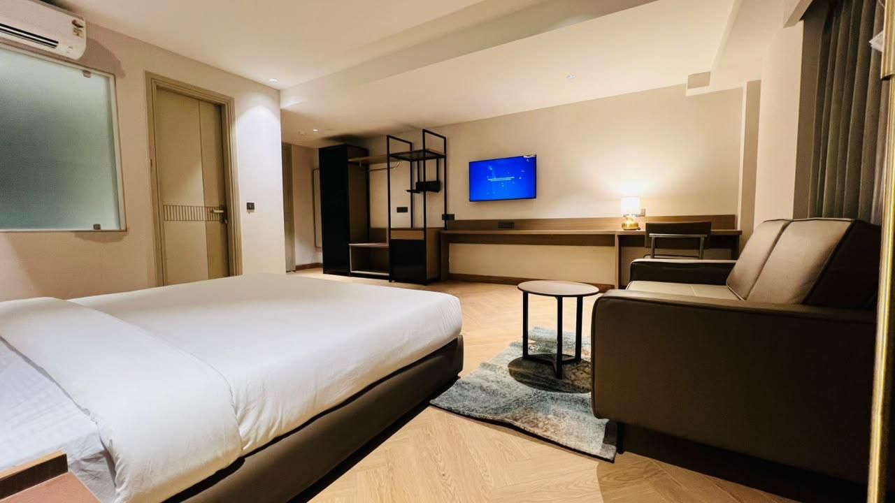 Habitación de hotel con cama, sofá, televisión y una mesita.