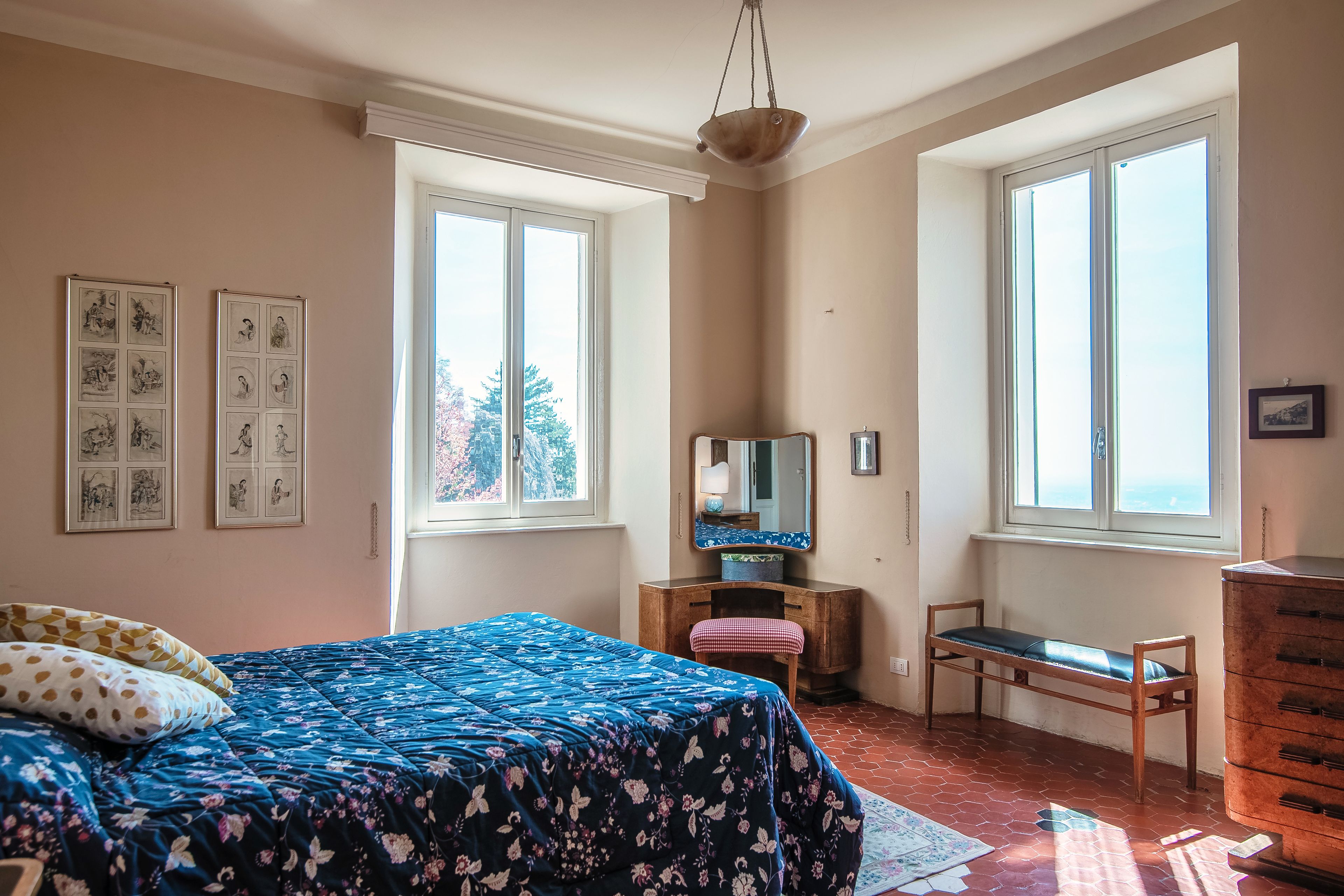 Une chambre à coucher avec un lit, une commode, une chaise, un miroir et des œuvres d’art accrochées au mur.