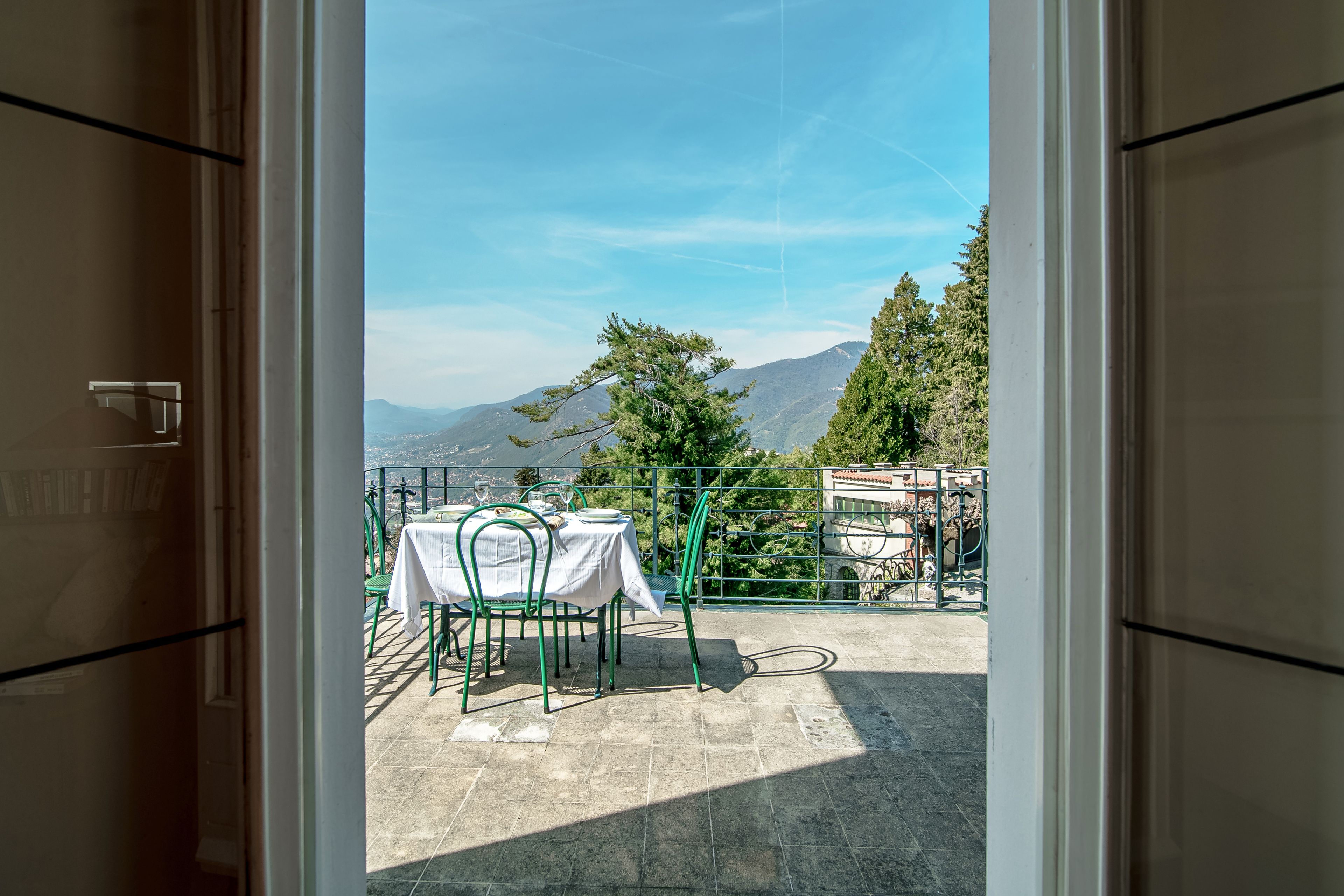A terrace with a table set for dining, overlooking a mountainous landscape.