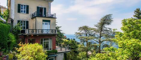 A multi-story building with a balcony, surrounded by lush greenery and overlooking a scenic landscape.