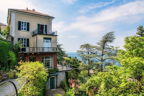 Un edificio de varios pisos con balcón, rodeado de exuberante vegetación y vistas a un paisaje pintoresco.
