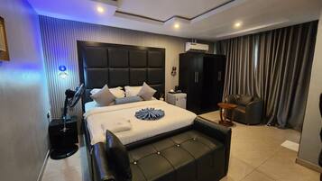 A modern bedroom with a large bed, a black leather sofa, an air conditioning unit, and a ceiling fan.