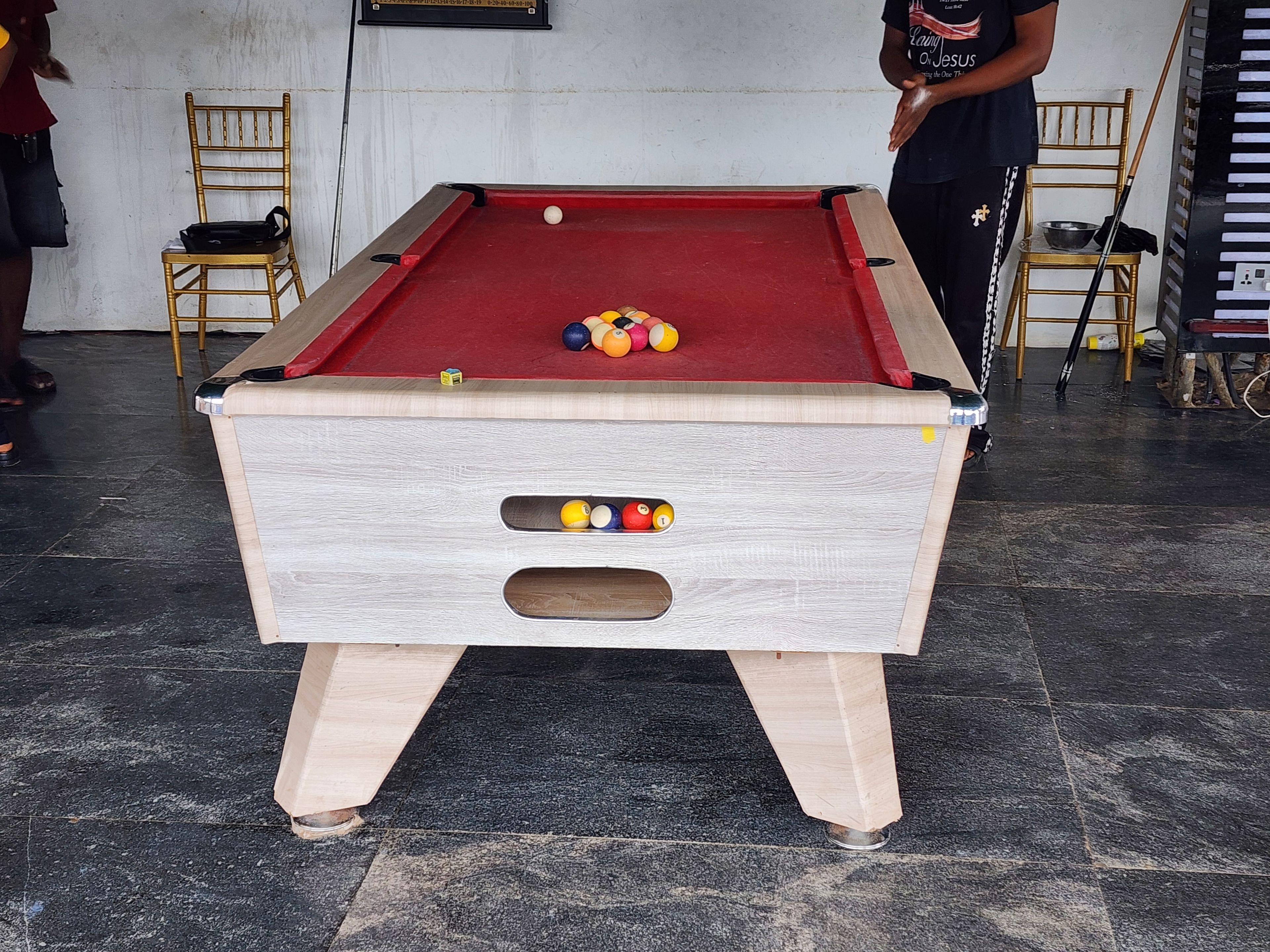 Una mesa de billar con bolas, sillas y un piano en una habitación con piso de baldosas.