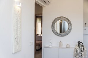 Ein Zimmer mit weißer Wand, einem runden Spiegel mit Zierrahmen, einem weißen Schrank mit Dekorationen und einer Tür zu einem anderen Raum.