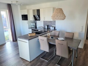 A modern kitchen with a central island, a dining area with chairs, and a hanging light fixture. - 50.3.n North Berth (Wangerland)