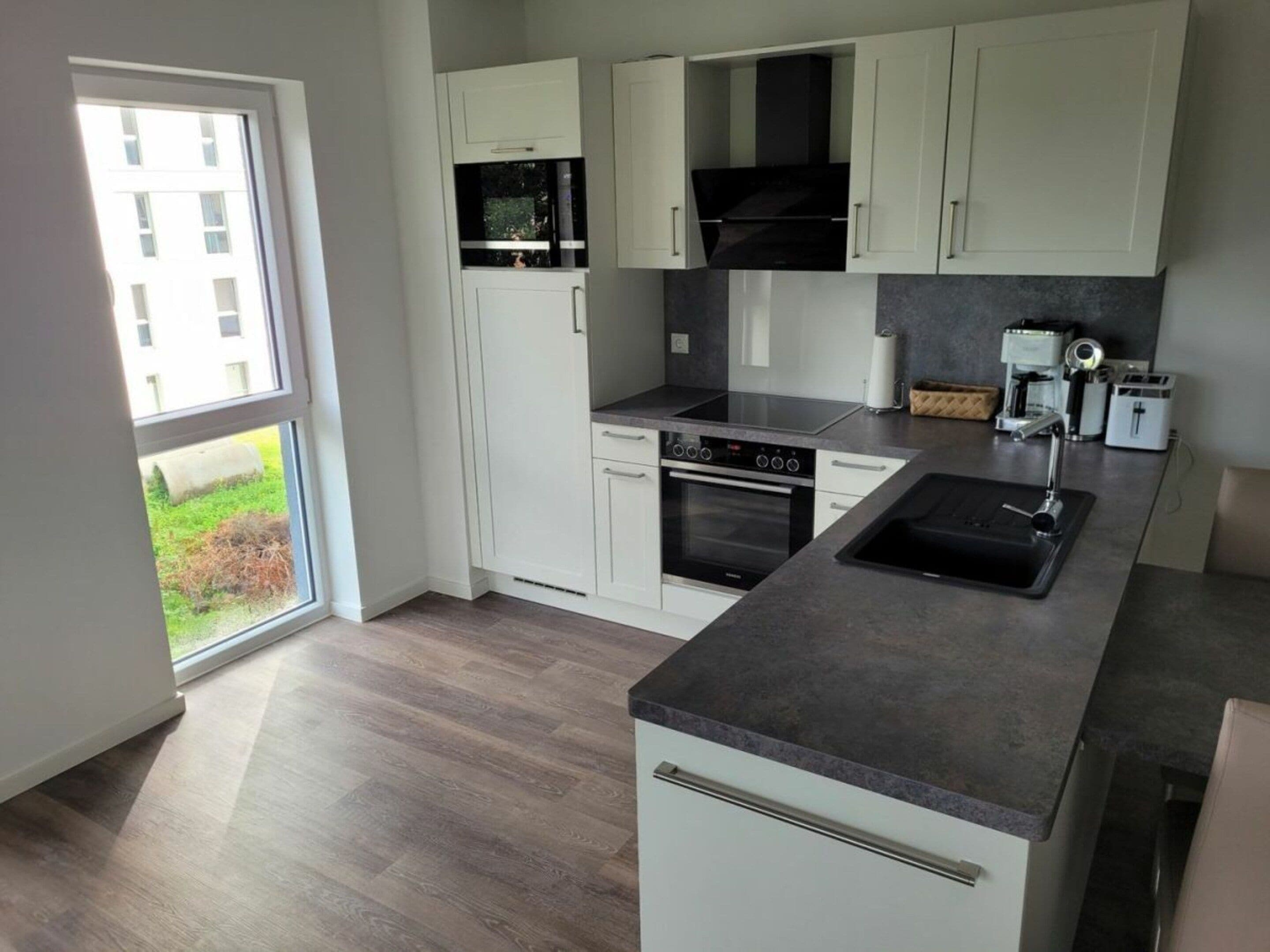 A modern kitchen with white cabinets, a black stove, and a large window.
