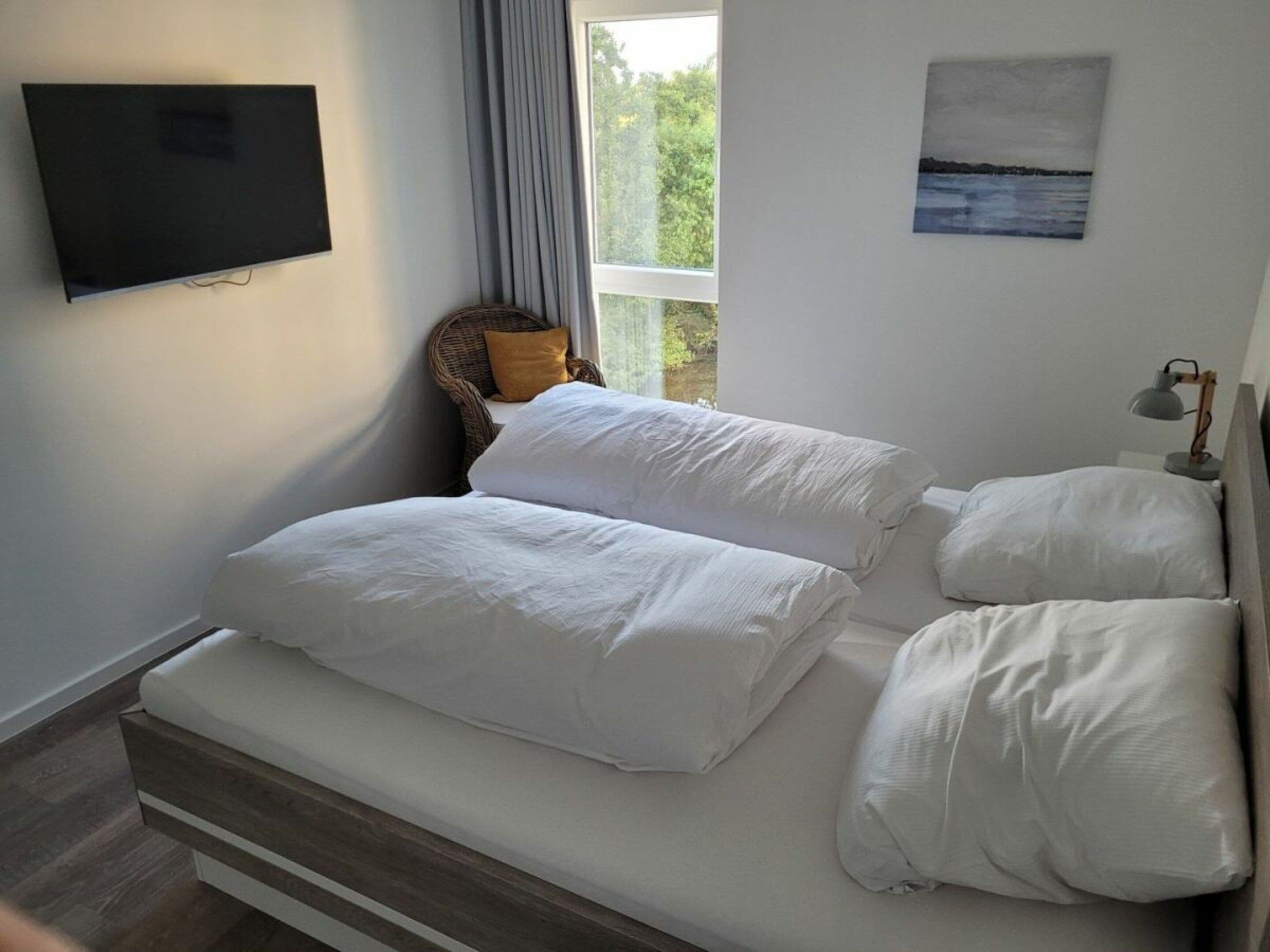 Ein Schlafzimmer mit einem Bett, einem Fernseher, einem Fenster mit Vorhängen und einem Gemälde an der Wand.