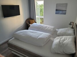 A bedroom with a bed, a television, a window with curtains, and a painting on the wall.