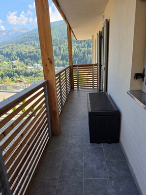 A balcony with a view of a forested mountain range, a wooden railing, and a bench. - Alba di Poggio al Sole Apartment in the Dolomites of Val di Sole (Mezzana)