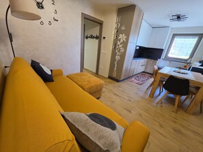 A living room with a sofa, a dining table, and a kitchen area. - Alba di Poggio al Sole Apartment in the Dolomites of Val di Sole (Mezzana)