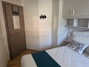 Ein Schlafzimmer mit einem Bett, einer Holztür, einem weißen Kleiderschrank und einem Nachttisch.