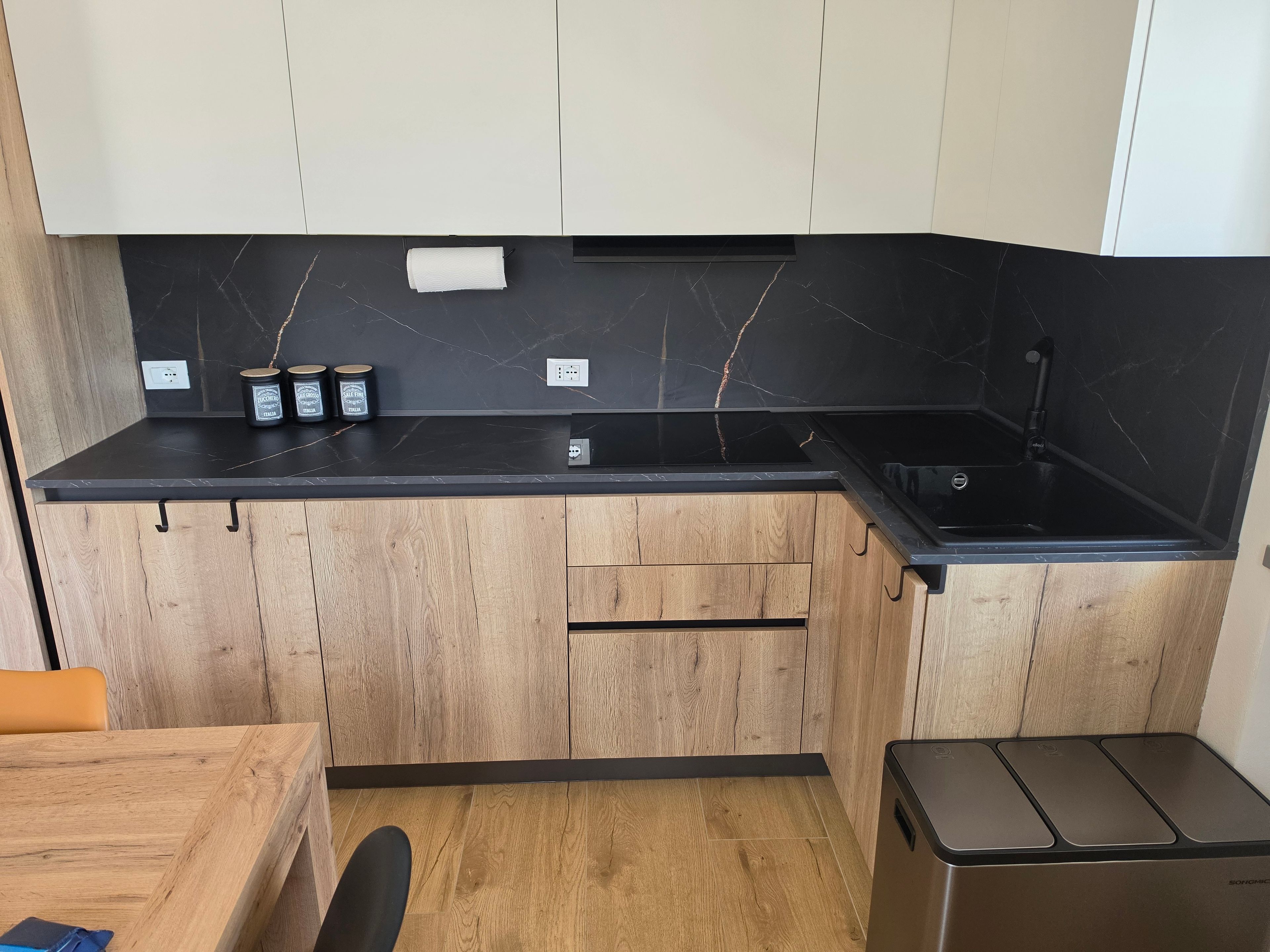 A compact kitchen with a black countertop, wooden cabinets, and a stainless steel dishwasher.