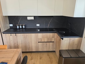 A compact kitchen with a black countertop, wooden cabinets, and a stainless steel dishwasher. - Alba di Poggio al Sole Apartment in the Dolomites of Val di Sole (Mezzana)