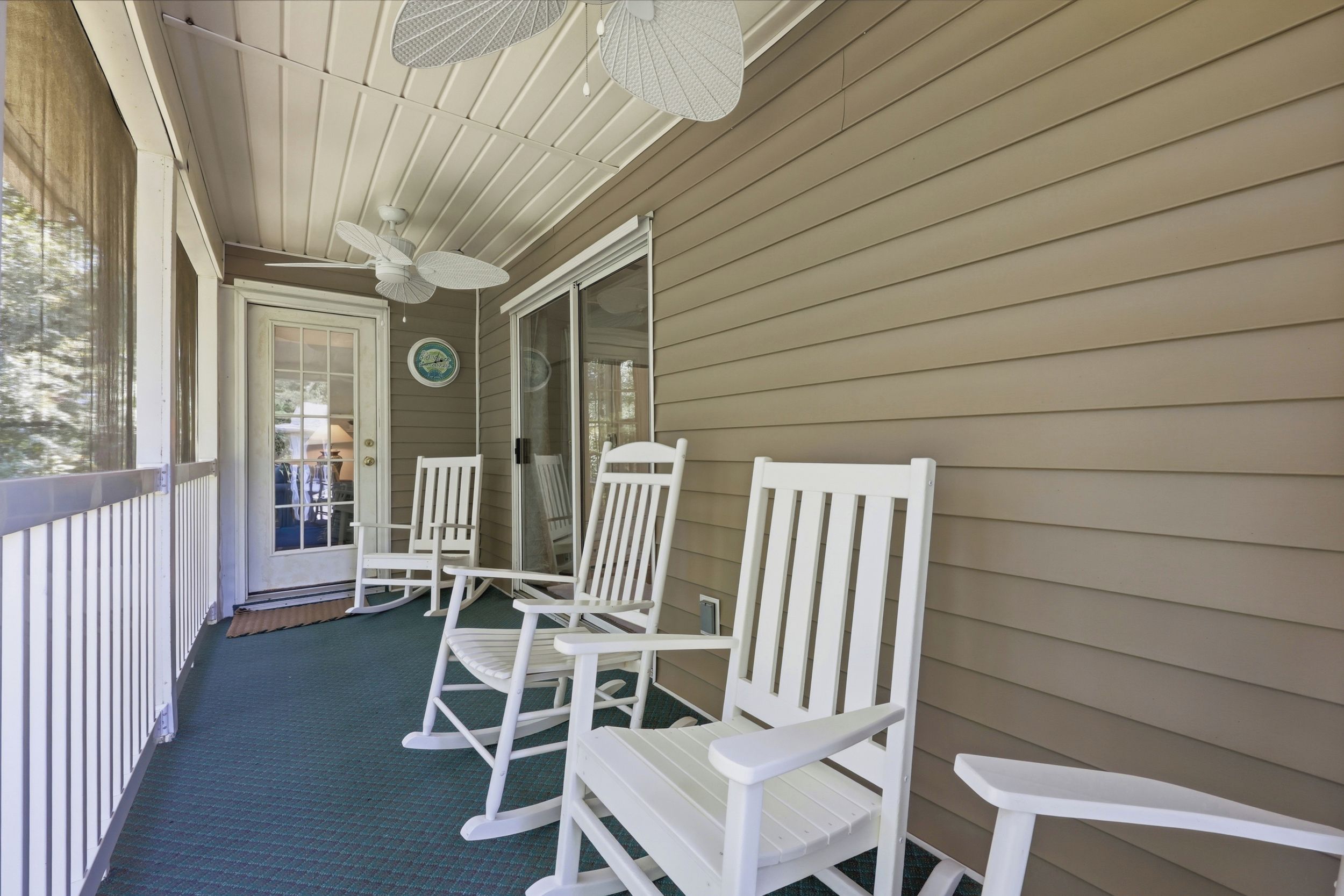 Een overdekte veranda met witte schommelstoelen, een plafondventilator en een glazen deur die naar een terras leidt.