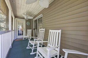 En inglasad veranda med vita gungstolar, en takfläkt och en glasdörr som leder ut till en uteplats.