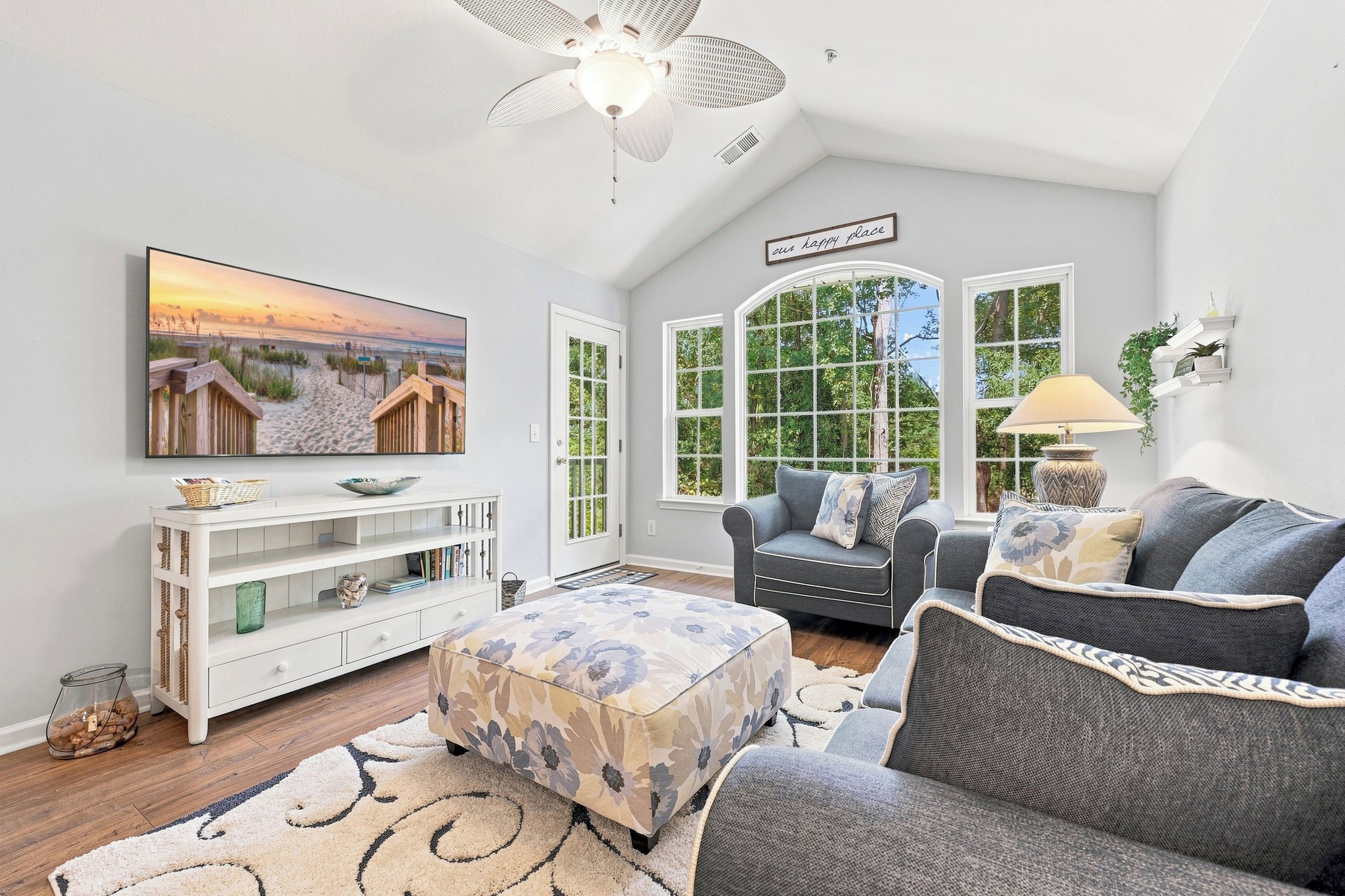 A living room with a television, a sofa, a chair, a decorative rug, and a ceiling fan.