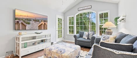 A living room with a television, a sofa, a chair, a decorative rug, and a ceiling fan.