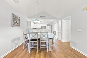 A modern kitchen with white cabinets, a hanging light fixture, and a dining area with a table and chairs. - 3 bedroom third floor condo with Golf Course View! (Pawleys Island)