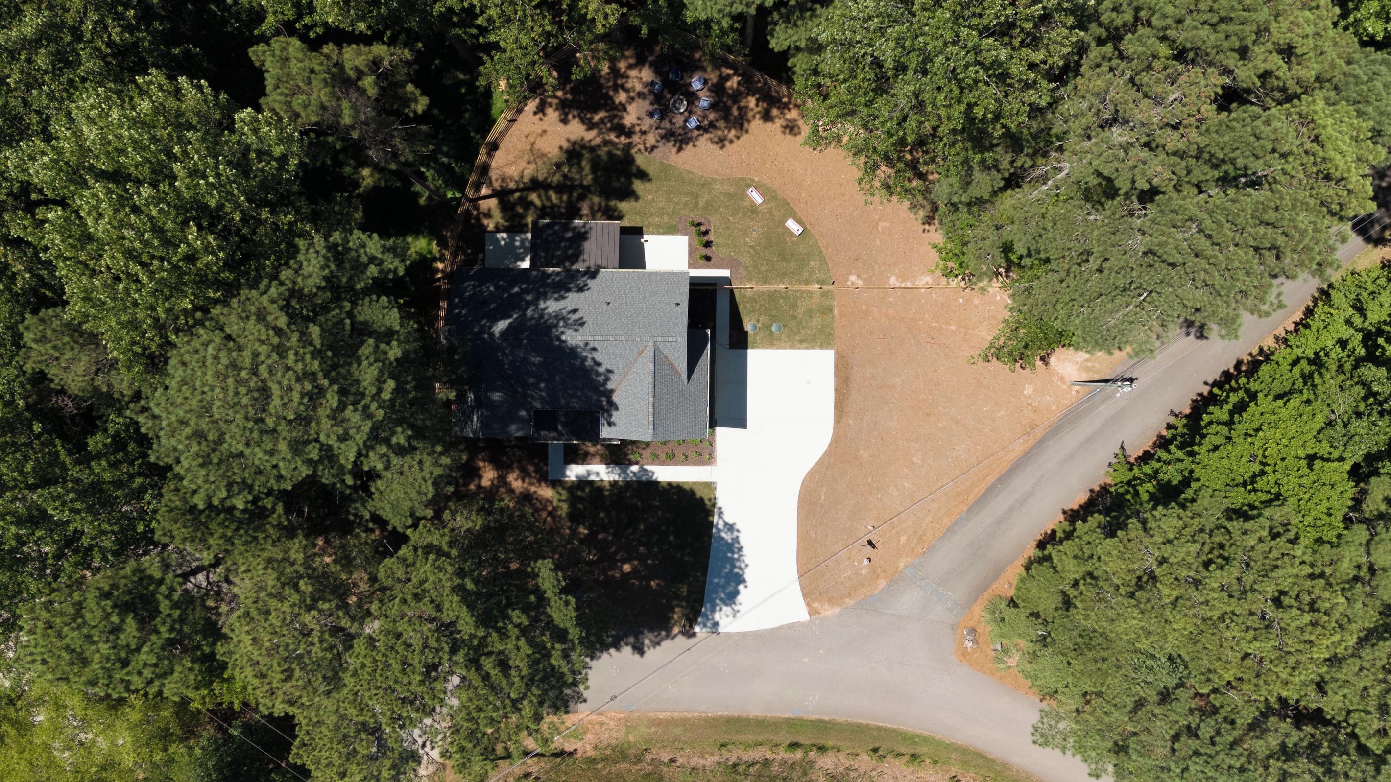 Une vue aérienne d’une maison entourée d’une forêt dense, avec une allée menant à l’entrée.