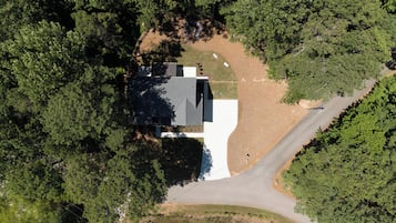 Une vue aérienne d’une maison entourée d’une forêt dense, avec une allée menant à l’entrée.