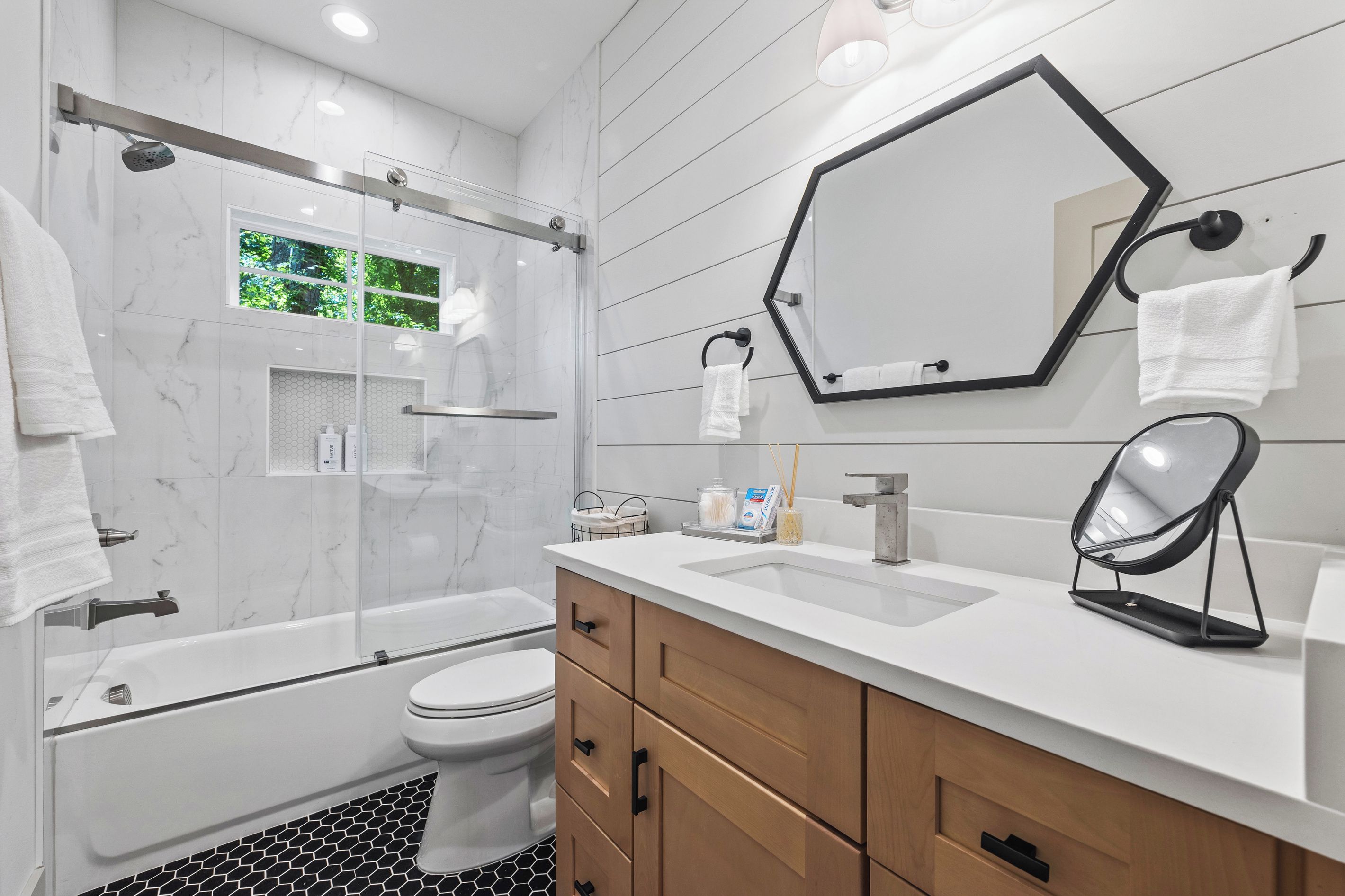 Een moderne badkamer met een glazen douchecabine, toilet, wastafel met spiegel en een bad.